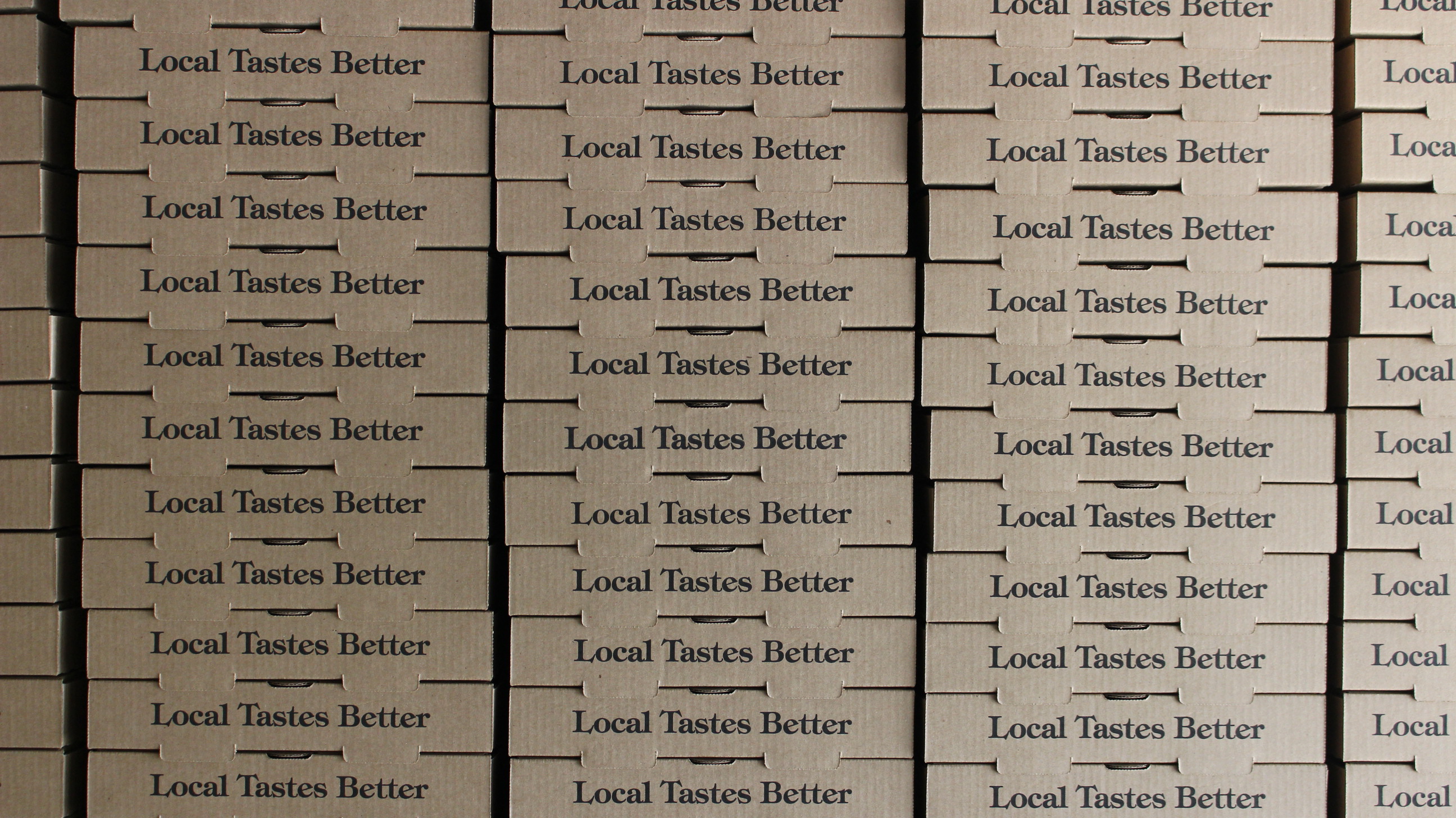 A wall of Harvest pizza boxes printed with "Local Tastes Better"