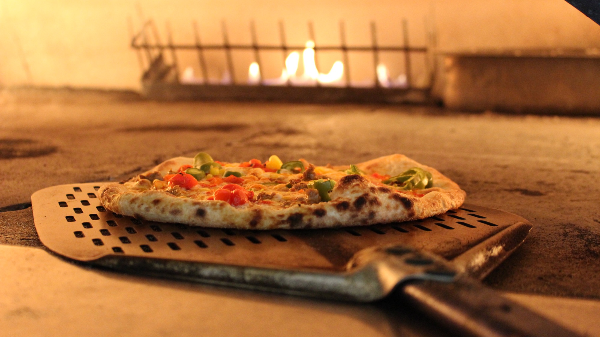 Wood-fired Harvest pizza on a peel in front of the oven flames