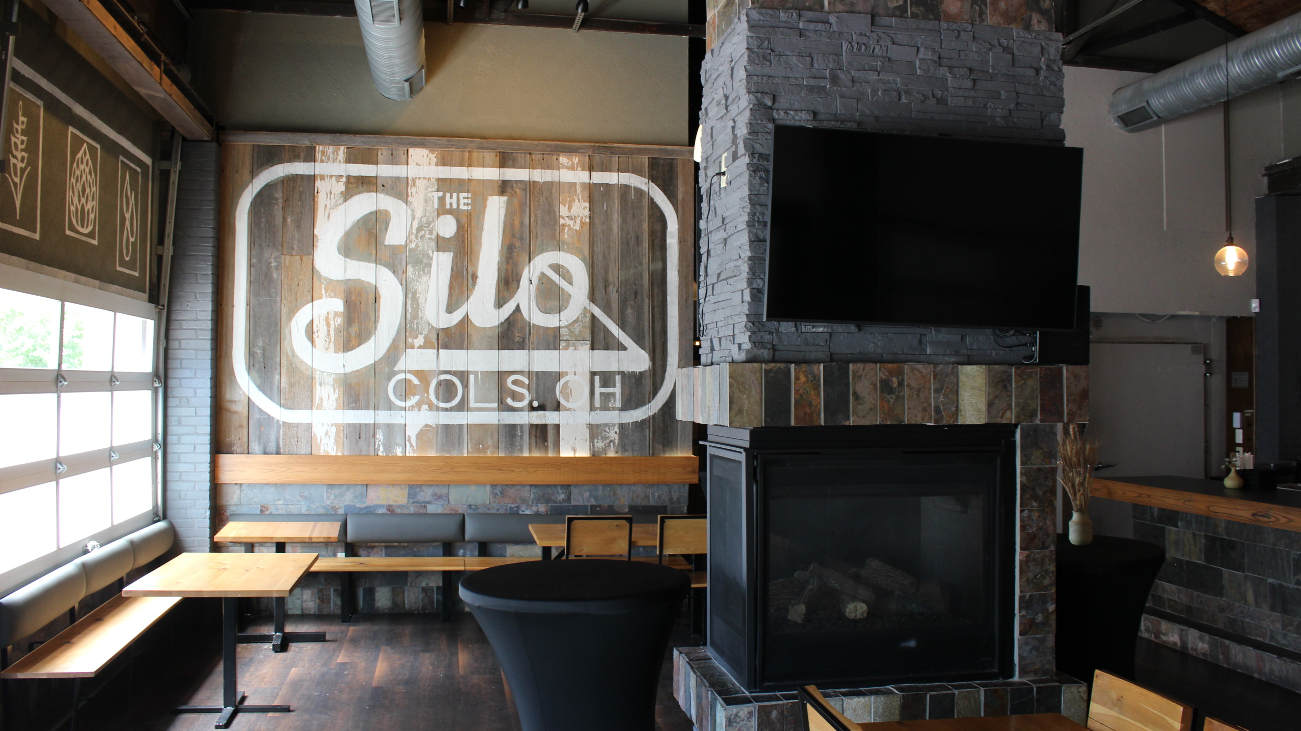 The Silo signature mural beside the stone fireplace and lounge seating at Harvest Brewery District